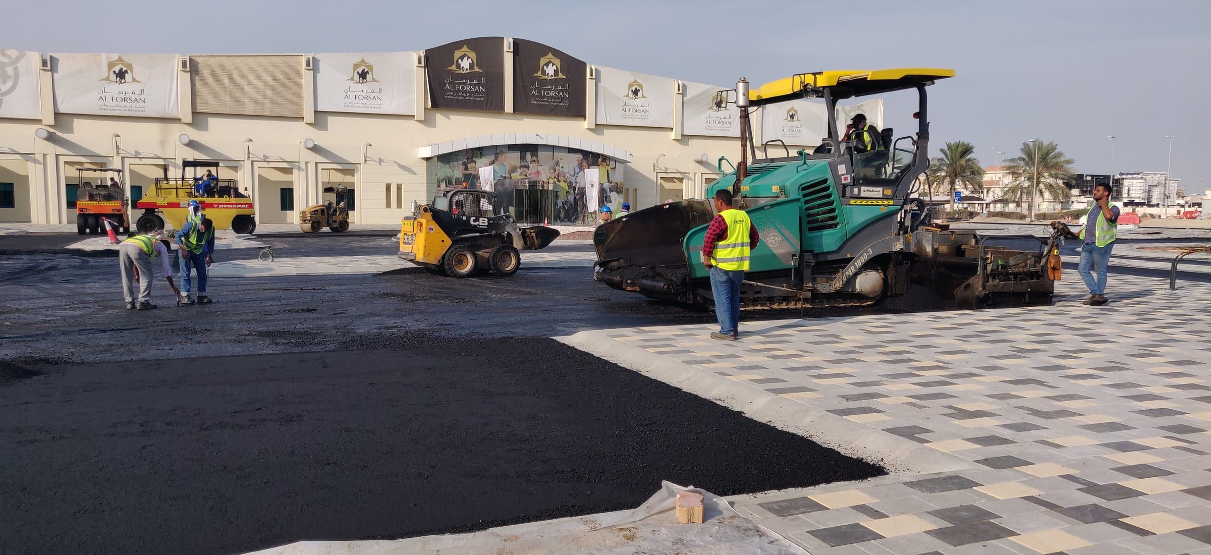 AIMS crew laying asphalt with a paver and rollers at Al Forsan