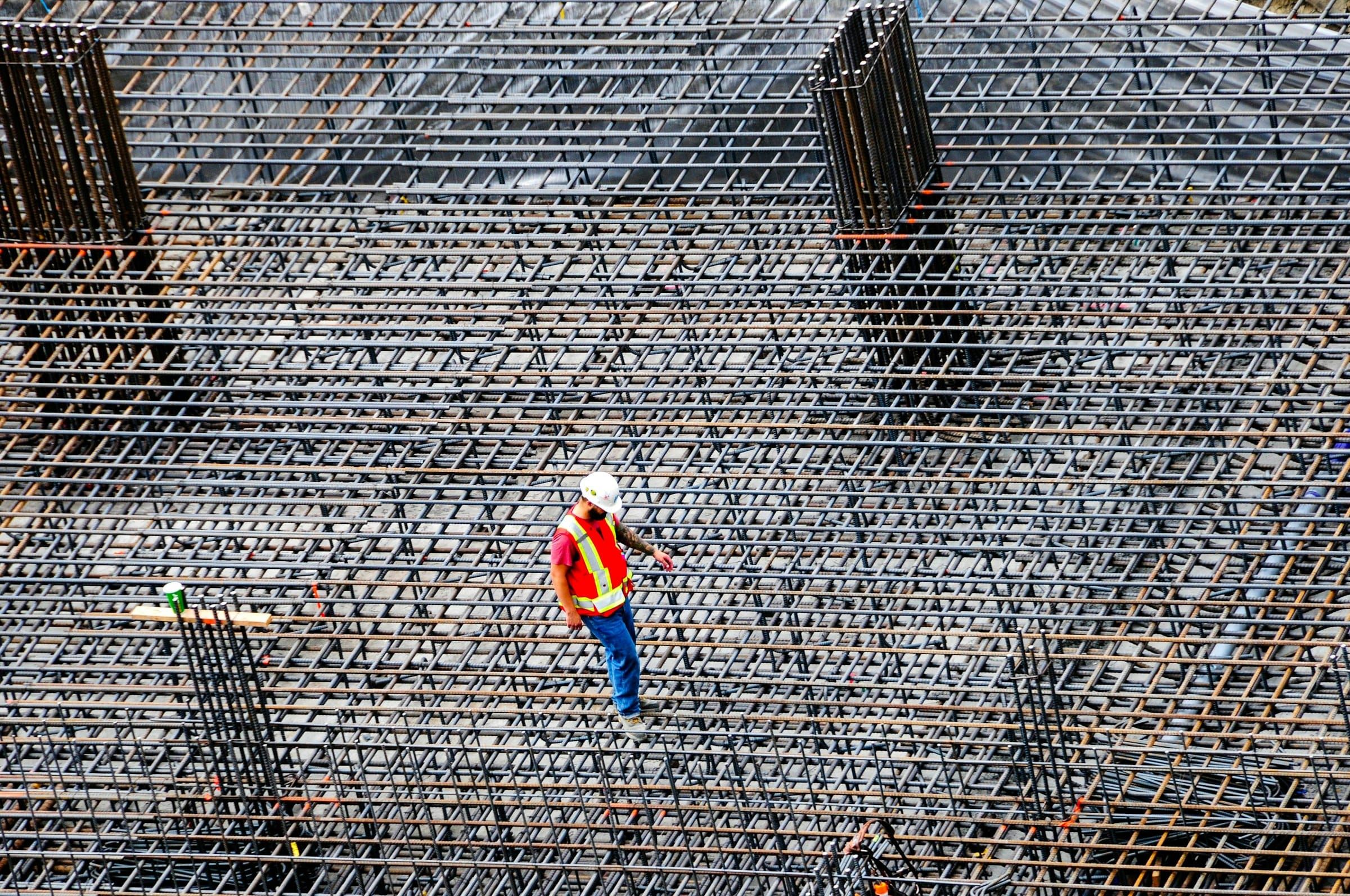 Engineer in a hard hat and high-visibility vest inspecting a reinforcement mat before a concrete pour